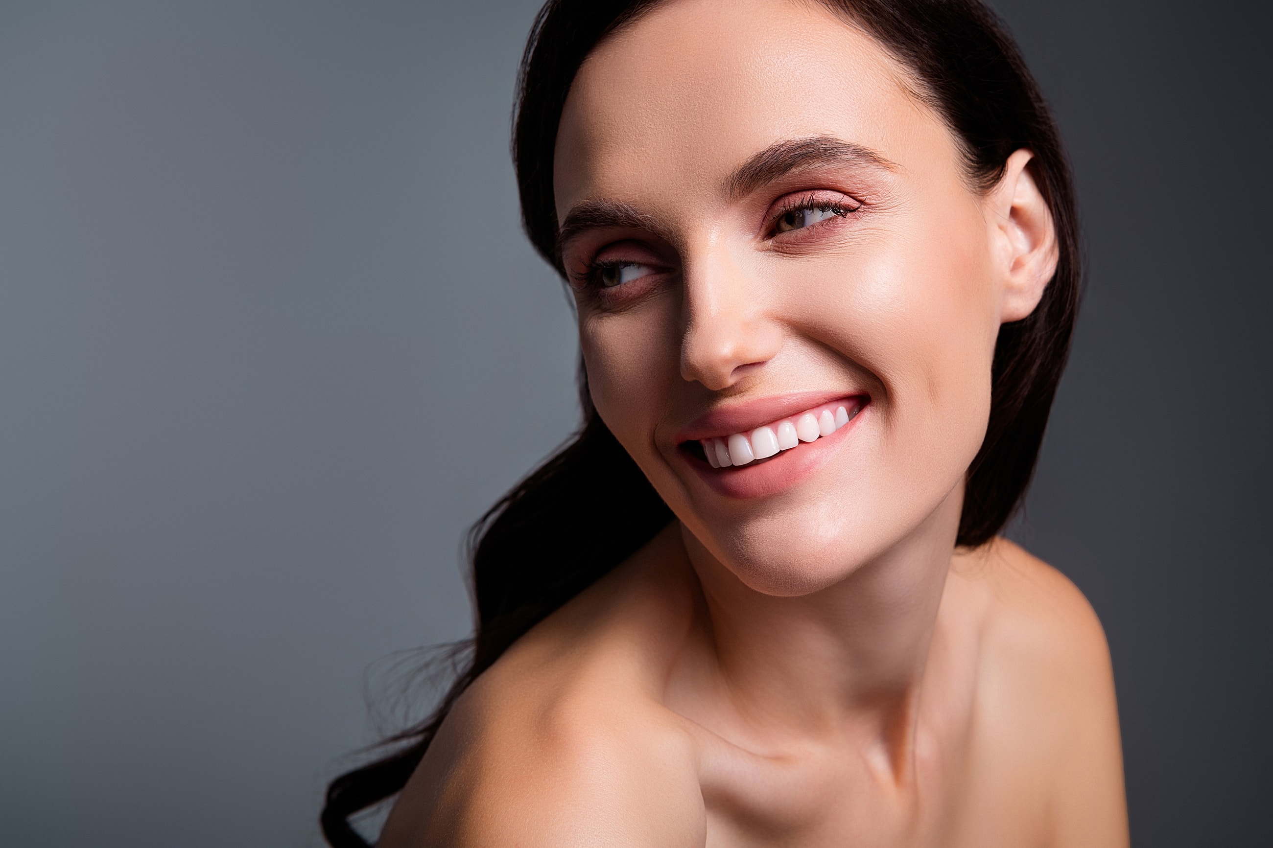 Smiling woman with natural makeup on gray background